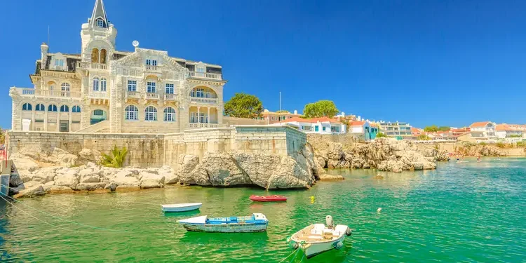 Scenic landscape of abandoned Palace Seixas and boats on the waterfront of Cascais, Lisbon Coast in Portugal. Praia da Rainha on the distance. Turquoise sea in summertime.