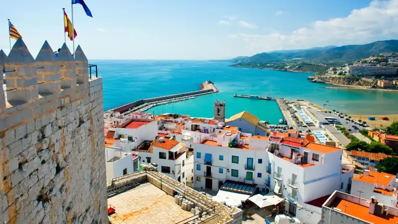 Valencian coastal town in Spain with white buildings, red roofs, and a harbor by turquoise sea.