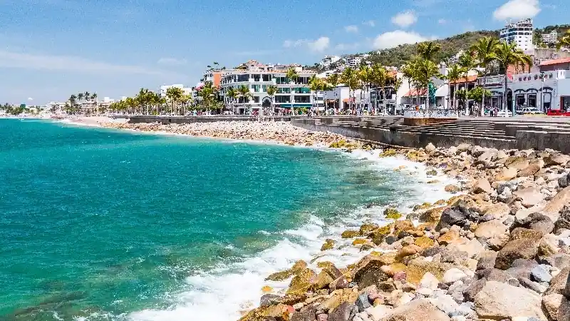 Coastal boardwalk in Puerto Vallarta with ocean waves and palm-lined buildings.