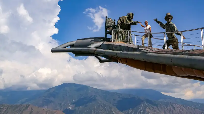 Panoramic view of a person on a part of Monument of the Virgin Mary soaring into the sky against blue sky and white clouds, Chicamocha Canyon, Colombia