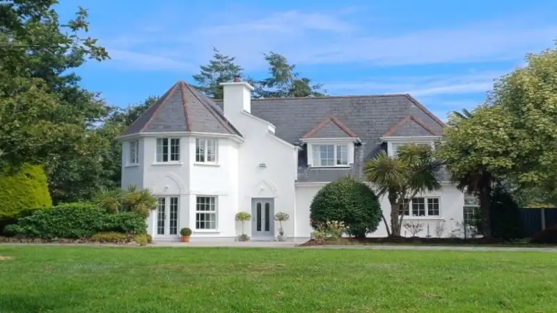 Large white two-story house with a gray roof surrounded by trees and a green lawn.