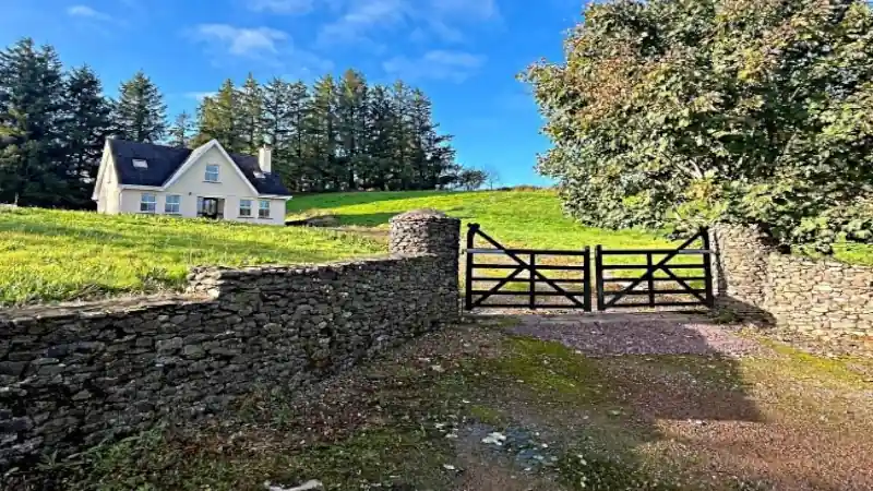 Country house behind a stone wall and wooden gate on a sunny day.