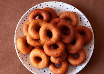 Plate of golden-brown rosquitas, a ring-shaped, crispy Panamanian pastry, stacked on a white dish with black speckles against a brown background.