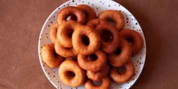 Plate of golden-brown rosquitas, a ring-shaped, crispy Panamanian pastry, stacked on a white dish with black speckles against a brown background.