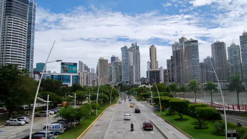 Panama City’s Avenida Balboa with cars on a coastal highway, lined with green parks and modern high-rise buildings under a partly cloudy sky.