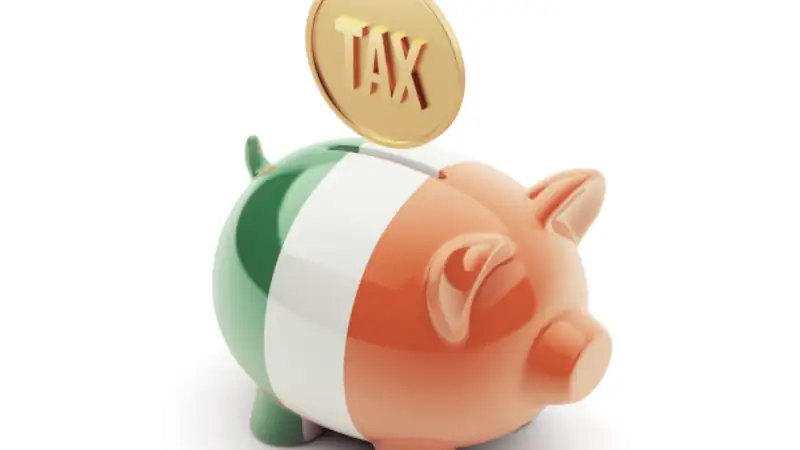 Piggy bank painted with Ireland’s flag and a gold coin labeled “TAX” being inserted on top.