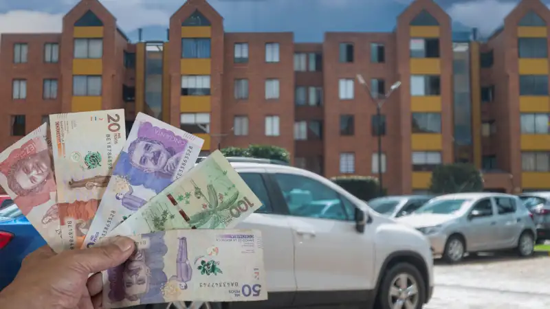 Colombian peso bills in a man's hand in front of a parking lot and apartment buildings.