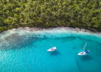 San Blas Islands, Panama - Aerial Drone Top Down View of two Sailing Yachts anchored in Turquoise Water right next to perfect White Sand Beach of Caribbean Tropical Island full of green Palm Trees.