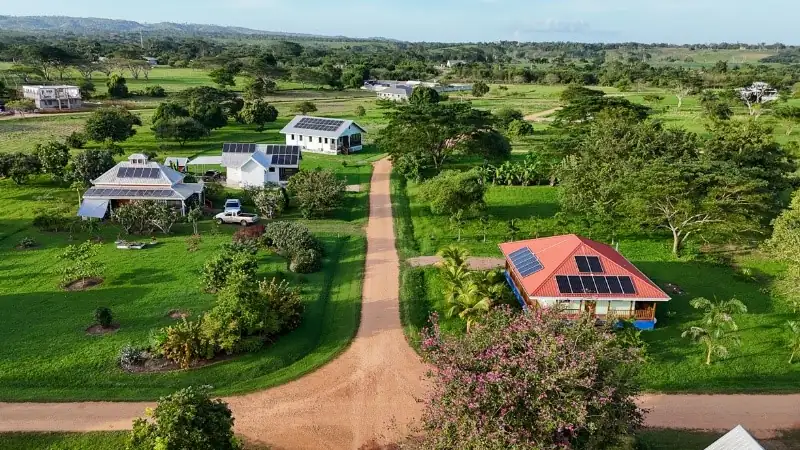Aerial view of a sustainable community featuring solar-powered homes and an active lifestyle set within lush, green tropical landscapes.