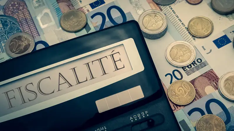 Calculator with the words "fiscalité" in French. In the background there are many euro bills and coins.