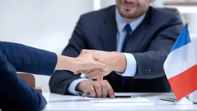 French official signing docs about state business support, shaking partner hand