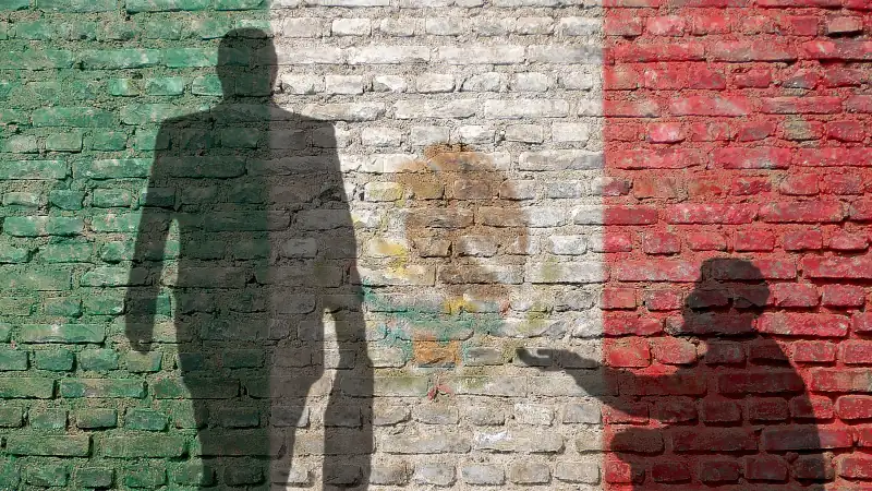 Two contrasting shadows appear on a wall painted with the Mexican flag. The difference in size symbolizes social and economic inequality in Mexico