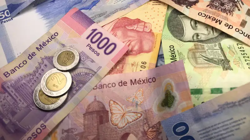 Many mixed Mexican peso bills spread over a wooden desk