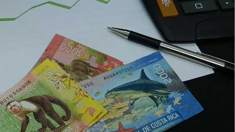 Costa Rica banknotes, pen and calculator on background with rising trend green line