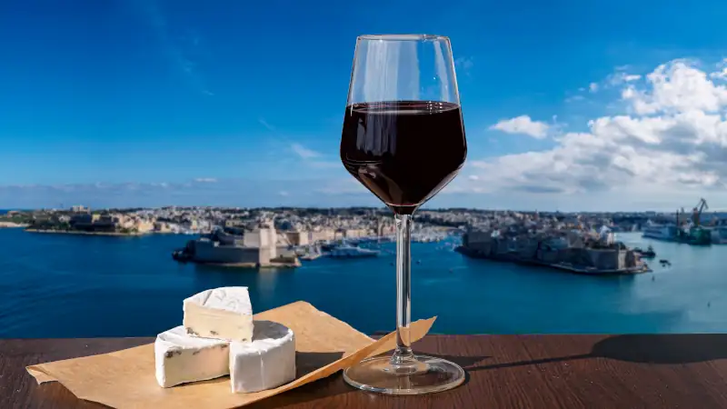 Glass of red wine with cheese with view of city wall and harbor in Valletta, Malta.