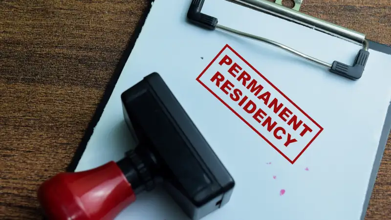 Red Handle Rubber Stamper and Permanent Residency text above book isolated on wooden background