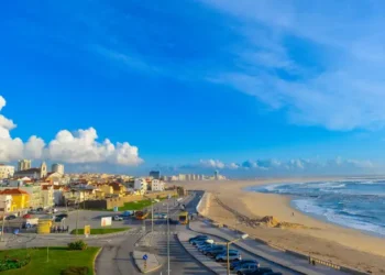 Sunny coastal cityscape in Portugal with colorful buildings, a sandy beach, rolling Atlantic waves, and a vivid blue sky.