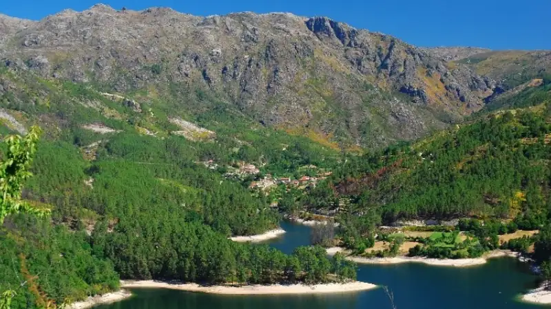 Scenic mountain landscape in Portugal, with forested hills, a winding lake, and a small village nestled in the valley.