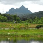 a small hut next to a lake and mountains surrounded by lush green grass