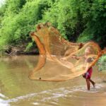 a boy casts his net for fishing in a river in Laos